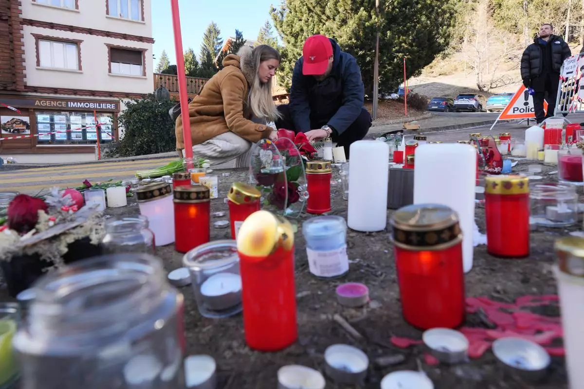 People bring flowers and candles near the sealed off Le Constellation bar, where a devastating fire left dead and injured during the New Year's celebrations in Crans-Montana, Swiss Alps, Switzerland, Friday, Jan. 2, 2026. (AP Photo/ Antonio Calanni)