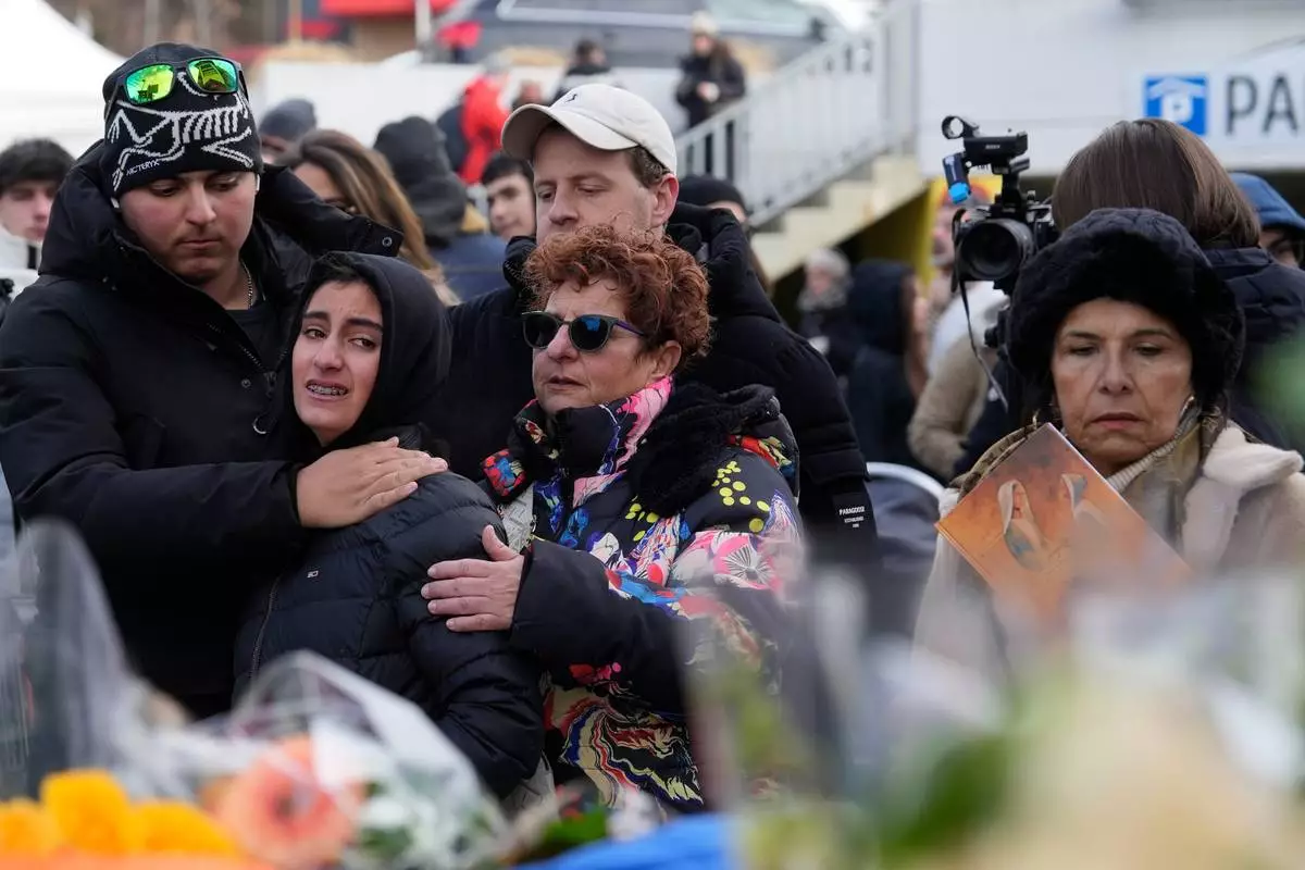 People mourn behind flowers near the sealed off Le Constellation bar, where a devastating fire left dead and injured during the New Year's celebrations in Crans-Montana, Swiss Alps, Switzerland, Friday, Jan. 2, 2026. (AP Photo/Baz Ratner)