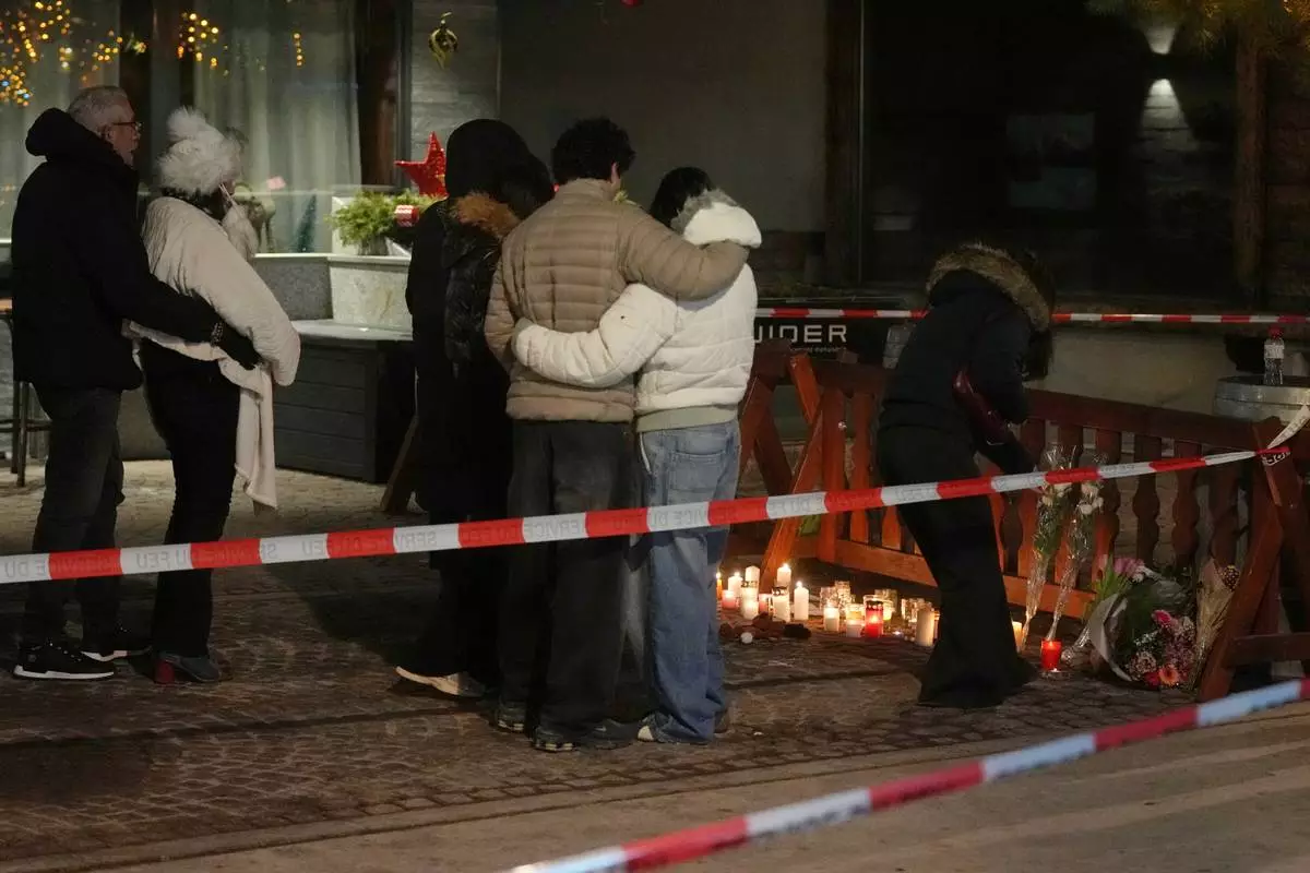 People lay candles and flowers near the Le Constellation bar, where a devastating fire left dead and injured during the New Year's celebrations in Crans-Montana, Swiss Alps, Switzerland, Thursday, Jan. 1, 2026. (AP Photo/ Antonio Calanni)