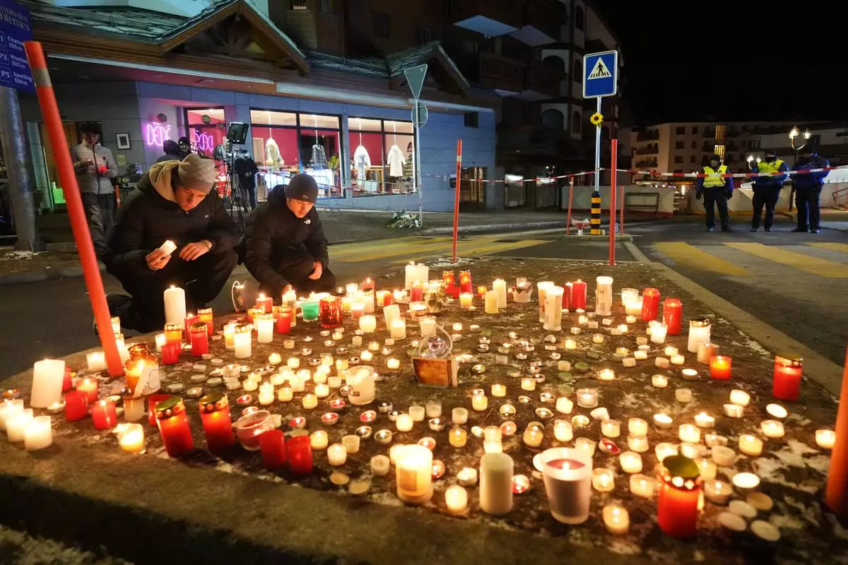 People lay candles near the Le Constellation bar, where a devastating fire left dead and injured during the New Year's celebrations in Crans-Montana, Swiss Alps, Switzerland, Thursday, Jan. 1, 2026. (AP Photo/ Antonio Calanni)