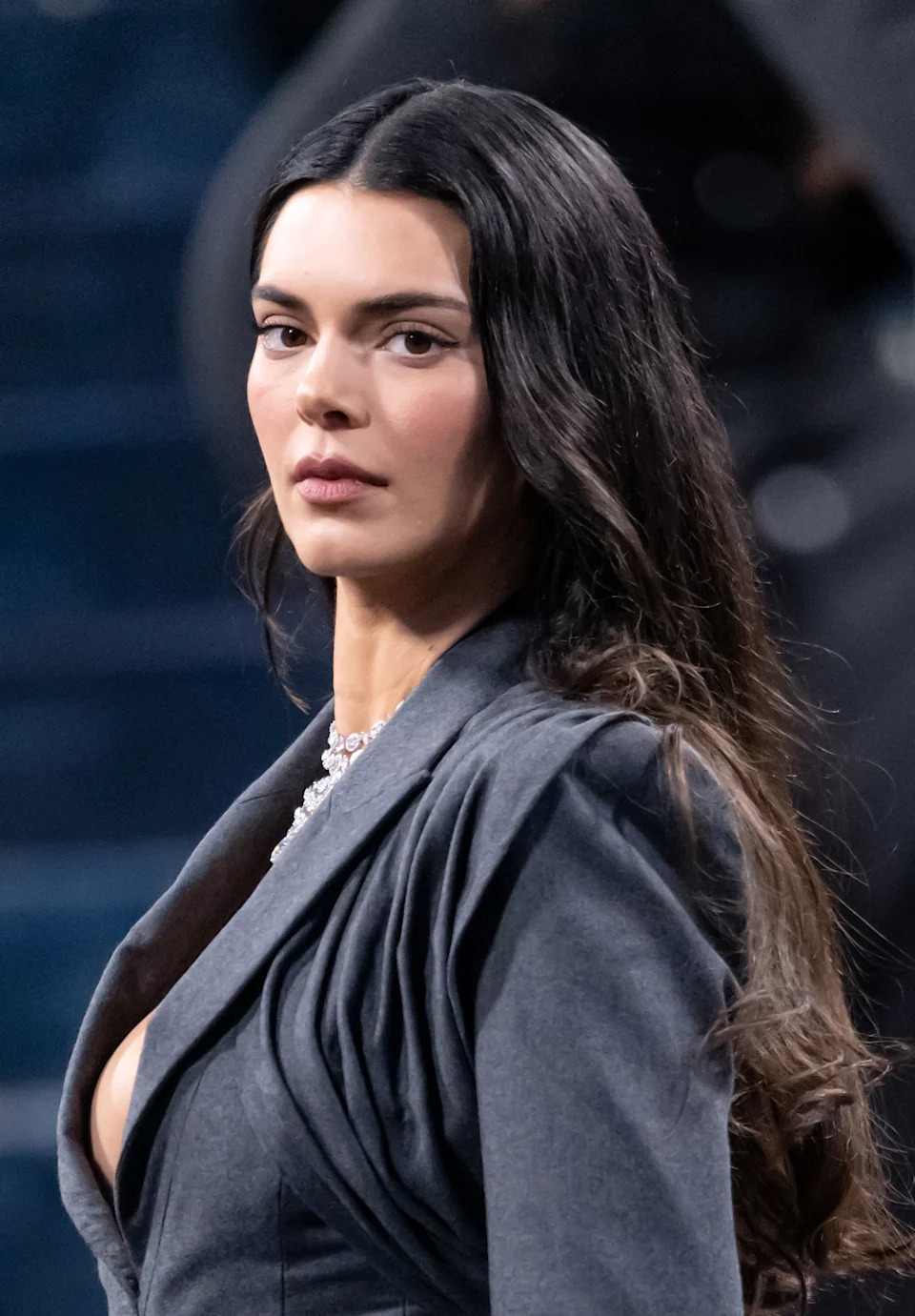 Kendall Jenner in an elegant, draped dress with long sleeves poses on red carpet