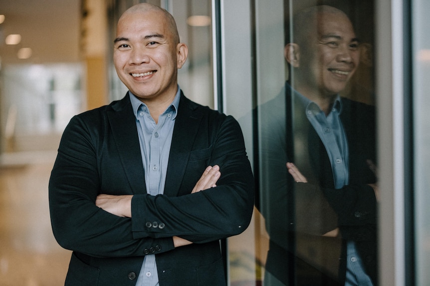 A man with his arms folded, leaning against a wall smiling for the camera.