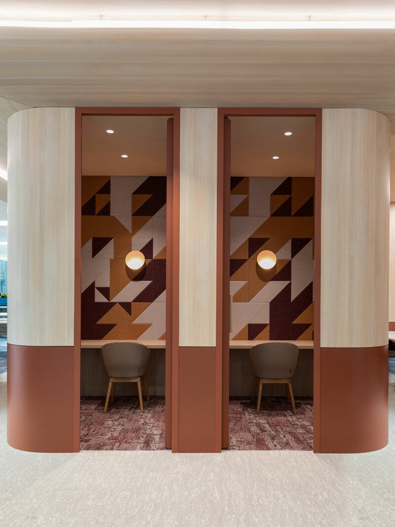 Two modern work nooks with wood paneling, geometric wall art, round light fixtures, and single beige chairs separated by a vertical divider.