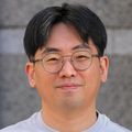 Junhoe Kim, Ph.D. (OHSU) Junhoe Kim, Ph.D., has short, black hair, eye glasses, and a gray shirt. He is smiling and standing outside the Vollum Institute.