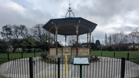 A bandstand in a London park surrounded by a black metal fence. 