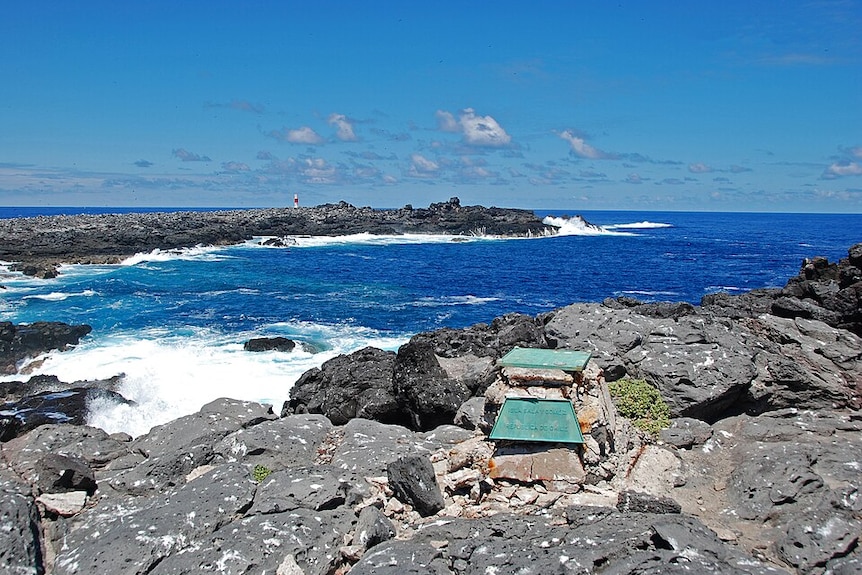 wide photo of a grey, rocky coastline with blue sea and sky behind.