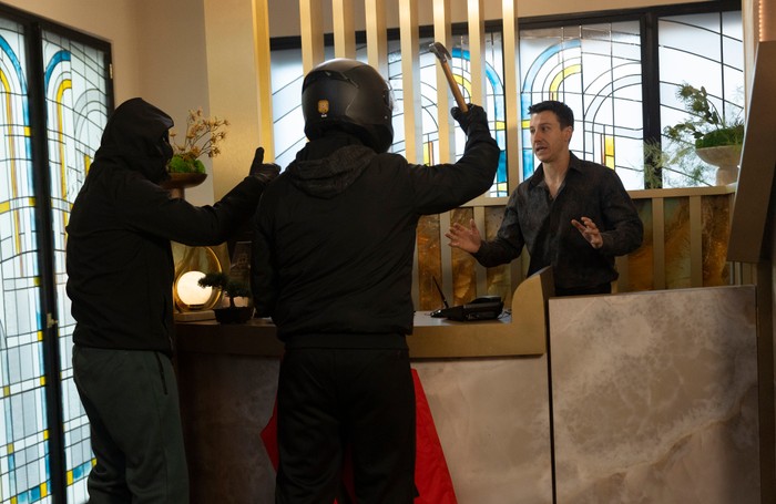 Ryan holds his hands in front of him as two masked robbers aim a claw hammer at him at the hotel reception desk in Coronation Street