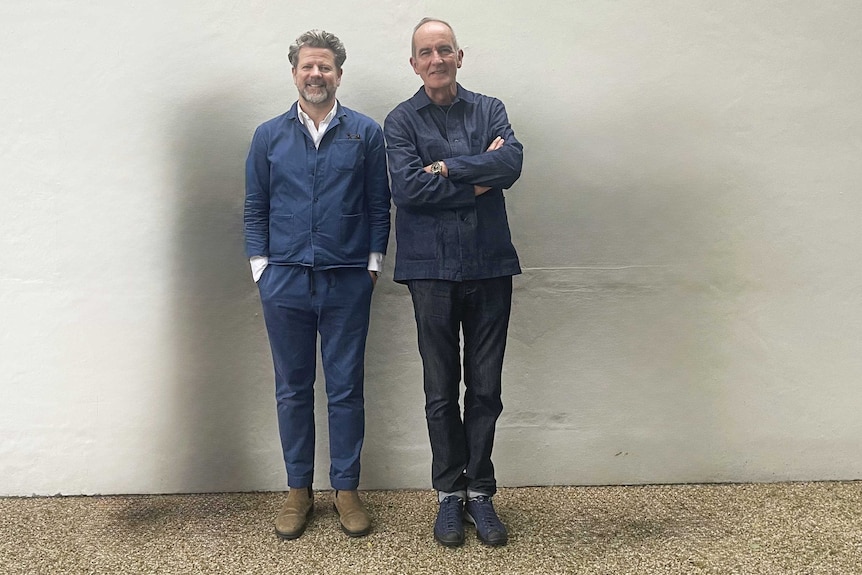 Kevina and Tim stands against a wall as they smile at the camera