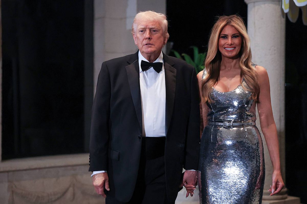 An individual in formal attire, comprising a black tuxedo and bow tie, accompanied by a woman dressed in a shimmering metallic gown, are seen strolling together on a formal event's venue.