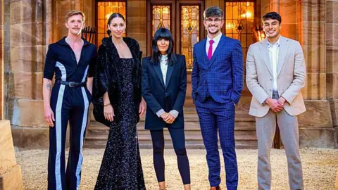 BBC/Studio Lambert/Paul Chappells Stephen, Rachel and Claudia standing outside the Traitors castle. This time they are joined by two other men. One is Jack, wearing a blue checked suit, a pink tie and glasses. He has his hands in his pockets. The other, Faraaz is wearing a beige suit and white shirt with his hands clasped in front of him.