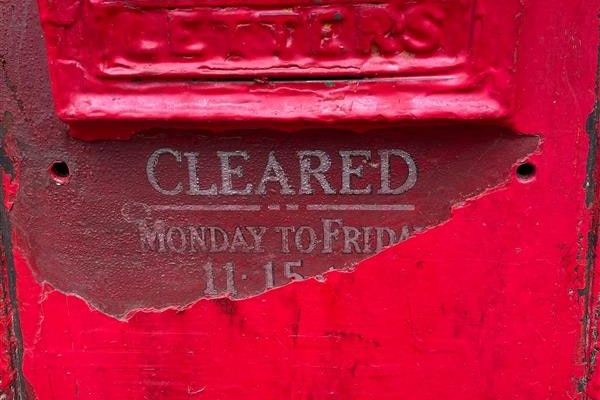 A post box clearance schedule is revealed from beneath a layer of red paint.