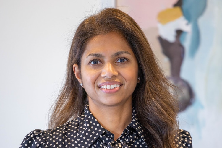 A woman with brown hair and a polka-dot shirt in front of a pastel painting.