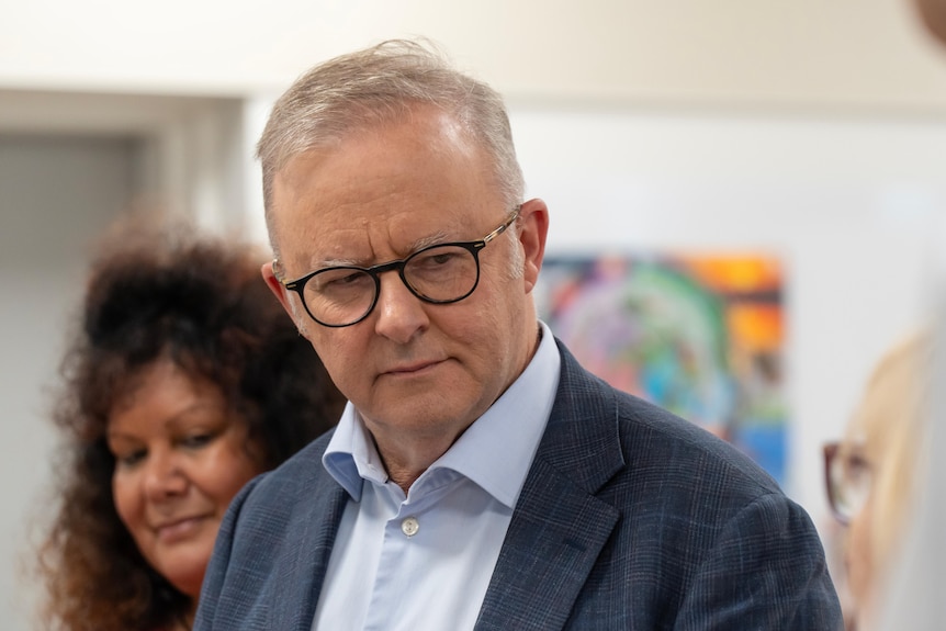 A close-up of Anthony Albanese looking serious while listening to someone speak, inside a room.