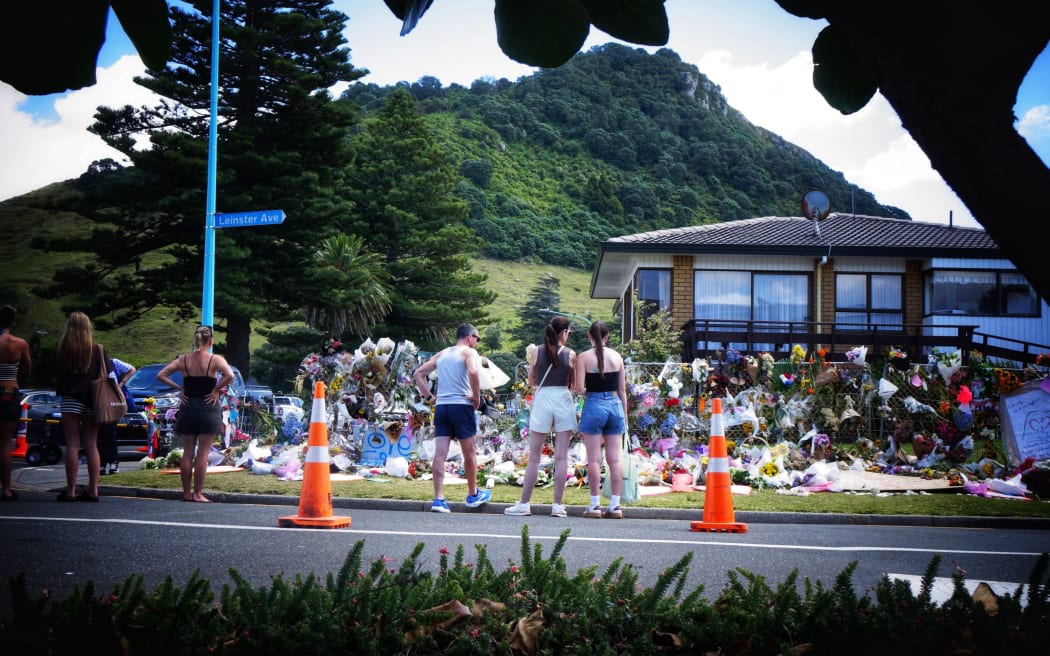 One week on, people reflect at a memorial site for the six people who died in a landslide in Mount Maunganui. Five remain missing and are yet to be recovered. Flowers and tributes adorn a wall near the cordon. Photo taken 29 January 2026.