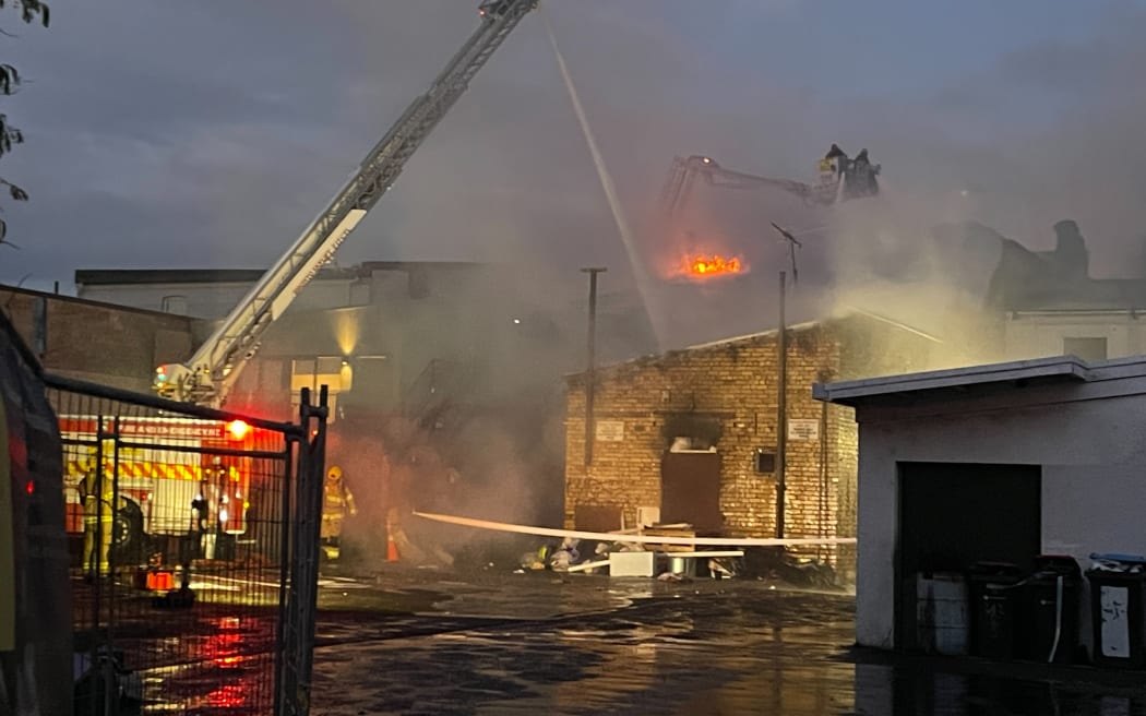 Flames could be seen over the top of an Onehunga building, as firefighters work from ladders, on Sunday night, 25 January, 2026.