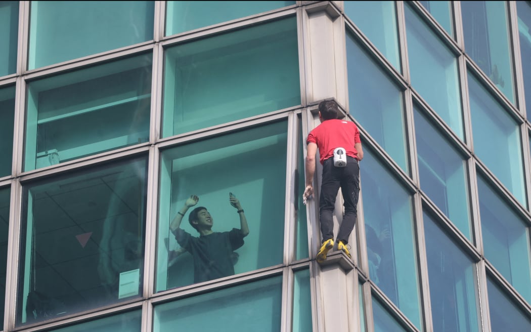 A building occupant uses his phone to record US rock climber Alex Honnold climbing the Taipei 101 building without ropes or safety gear in Taipei on January 25, 2026. (Photo by I-Hwa Cheng / AFP)