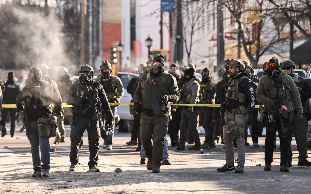 Federal agents stand near police tape as demonstators gather near the site of where state and local authorities say a man was shot by federal agents earlier in the morning in Minneapolis, Minnesota, on January 24, 2026. Minnesota Governor Tim Walz said Saturday that federal agents deployed in Minneapolis as part of a sweeping immigration crackdown had carried out 