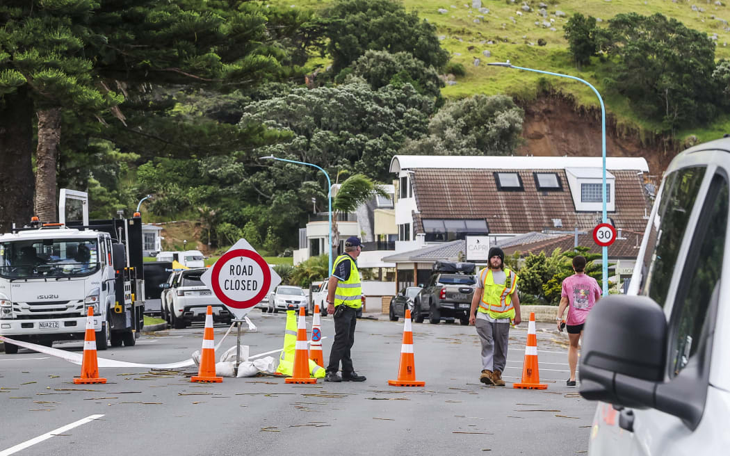 Emergency workers close a road following a landslide while a search is underway by local emergency services for missing people at Mount Maunganui in Tauranga on January 22, 2026. A landslide smashed into a campsite in rain-swept northern New Zealand leaving multiple people missing, police and rescuers said. (Photo by DJ MILLS / AFP)