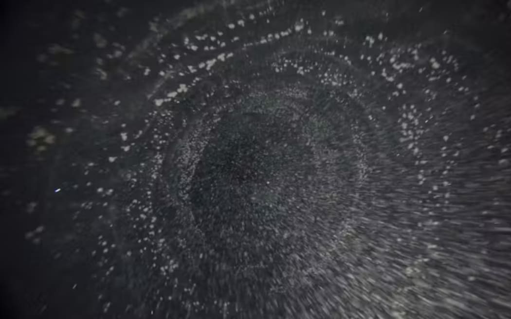 Looking downward in the borehole just before emerging into the ocean cavity. The white specks are sediment particles. Stevens/NIWA/K061, CC BY-NC-ND