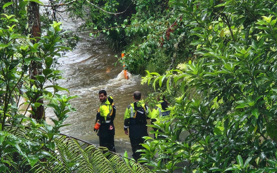 Police inspect a section of Falls Road near the Mahurangi River where a person and their vehicle is believed to have been swept into the river