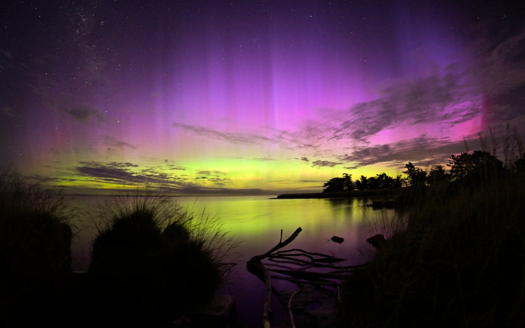 The Aurora Australis, also known as the Southern Lights, glows on the horizon over the waters of Lake Ellesmere on the outskirts of Christchurch, New Zealand, on January 21, 2026. The Southern Lights are a natural phenomenon of vibrant natural lights. Solar activity, particularly a coronal mass ejection that sends charged particles and gas into space, causes it. It typically takes these particles three days to reach the magnetic field lines at the north and south poles before entering the atmosphere. Upon entering, the energy and particles combine with atmospheric gases to create a spectrum of colored lights in the sky. (Photo by Sanka Vidanagama/NurPhoto) (Photo by SANKA VIDANAGAMA / NurPhoto via AFP)