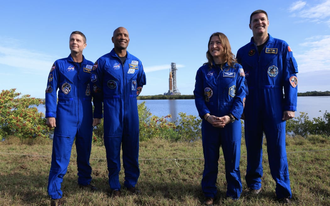 CAPE CANAVERAL, FLORIDA - JANUARY 17: (L-R) NASA's Artemis II Commander Reid Wiseman, pilot Victor Glover, mission specialist Christina Koch, and Jeremy Hansen pose for a photo as NASA's Artemis II (behind them) is rolled from the Vehicle Assembly Building to Launch Pad 39B at NASA’s Kennedy Space Center on January 17, 2026 in Cape Canaveral, Florida. NASA’s integrated SLS (Space Launch System) rocket and Orion spacecraft for the Artemis II mission are being rolled to Launch Pad 39B ahead of the 10-day mission in February 2026, which will take the crew around the Moon and back to Earth. Joe Raedle/Getty Images/AFP (Photo by JOE RAEDLE / GETTY IMAGES NORTH AMERICA / Getty Images via AFP)