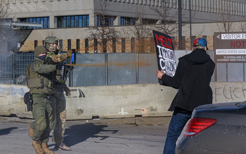 Federal agents use pepper spray against a protester holding a sign during an enforcement operation outside the Whipple Building, ICE facility in Minneapolis, Minnesota, on January 11, 2026. A US Immigration and Customs Enforcement (ICE) agent shot and killed 37-year-old Renee Nicole Good on the streets of Minneapolis on January 7, leading to huge protests and outrage from local leaders who rejected White House claims she was a domestic terrorist. (Photo by Kerem YUCEL / AFP)