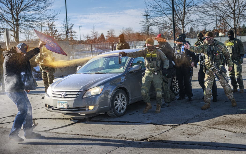 Federal agents use pepper spray against a protester holding a sign during an enforcement operation outside the Whipple Building, ICE facility in Minneapolis, Minnesota, on January 11, 2026. A US Immigration and Customs Enforcement (ICE) agent shot and killed 37-year-old Renee Nicole Good on the streets of Minneapolis on January 7, leading to huge protests and outrage from local leaders who rejected White House claims she was a domestic terrorist. (Photo by Kerem YUCEL / AFP)