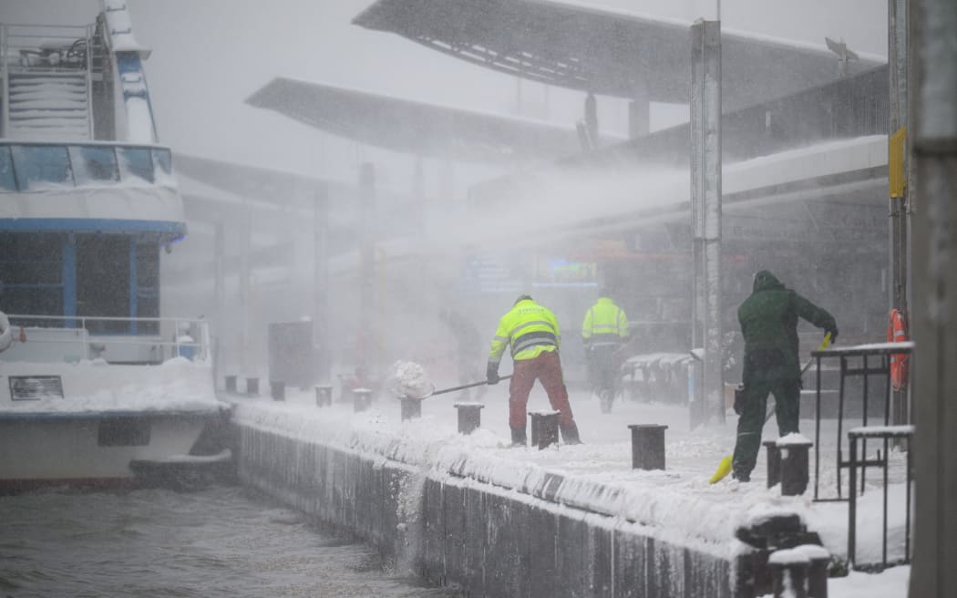 Workers clear snow and push it into the Elbe river during heavy snowfall at Landungsbruecken in Hamburg, Germany, on January 9, 2026. Storm Elli has arrived in northern Germany with heavy winds and snow. (Photo by DANIEL REINHARDT / AFP)