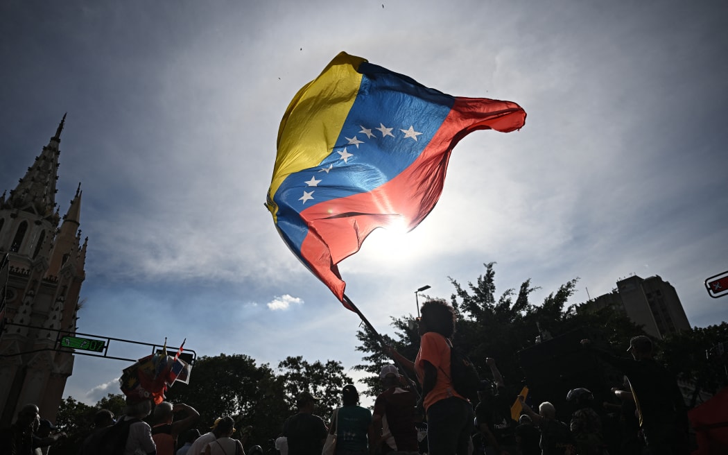 A person flutters a national flag in Caracas on January 3, 2026, after US forces captured Venezuelan leader Nicolas Maduro. President Donald Trump said Saturday that US forces had captured Venezuela's leader Nicolas Maduro after bombing the capital Caracas and other cities in a dramatic climax to a months-long standoff between Trump and his Venezuelan arch-foe. (Photo by Federico PARRA / AFP)