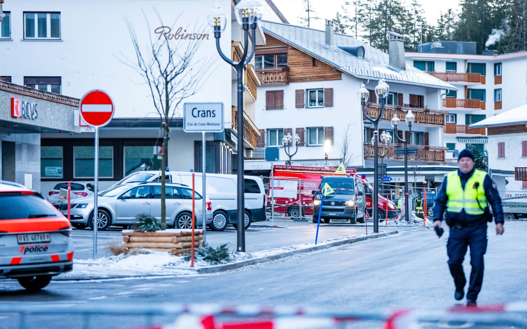 A police officer walks near ambulances at the site of an explosion that ripped through a bar in Crans-Montana on January 1, 2026. Several people were killed and others injured when an explosion ripped through a bar in the luxury Alpine ski resort town of Crans Montana, Swiss police said early on January 1. (Photo by MAXIME SCHMID / AFP)