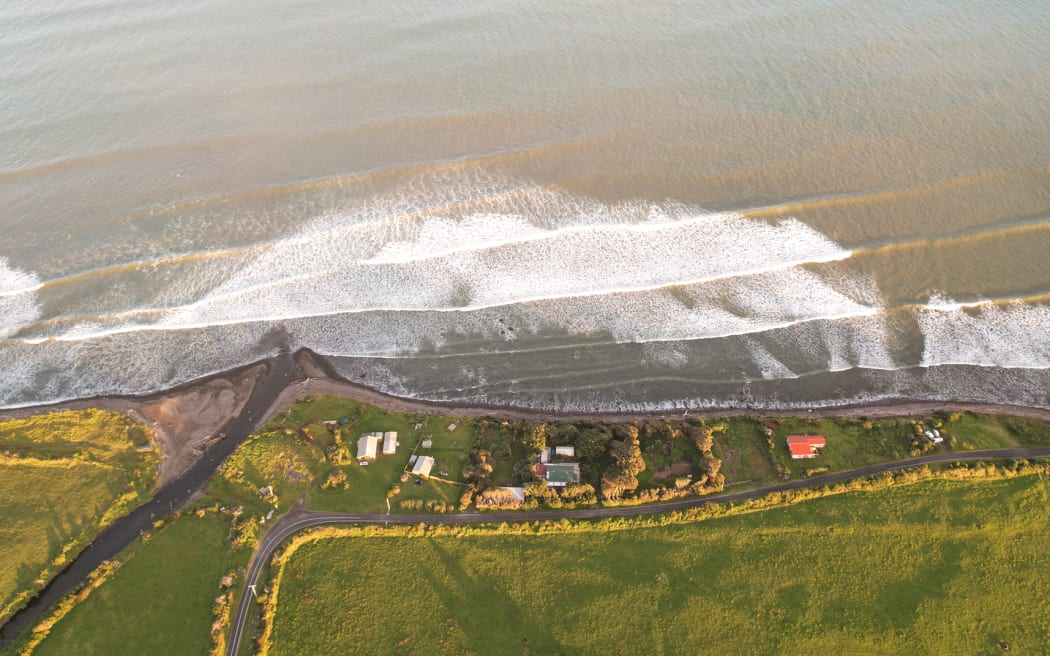 A drone shot above coastal water showing clear blue water at the top and brown, sediment-laden water at the bottom
