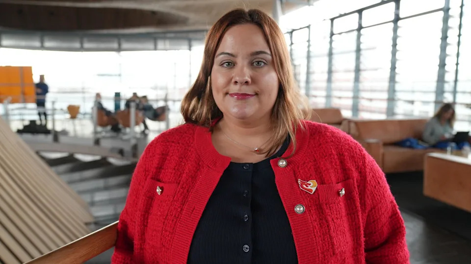 Angela Contestabile, who has brown hair and wears a red cardigan, stands in the Senedd in Cardiff Bay
