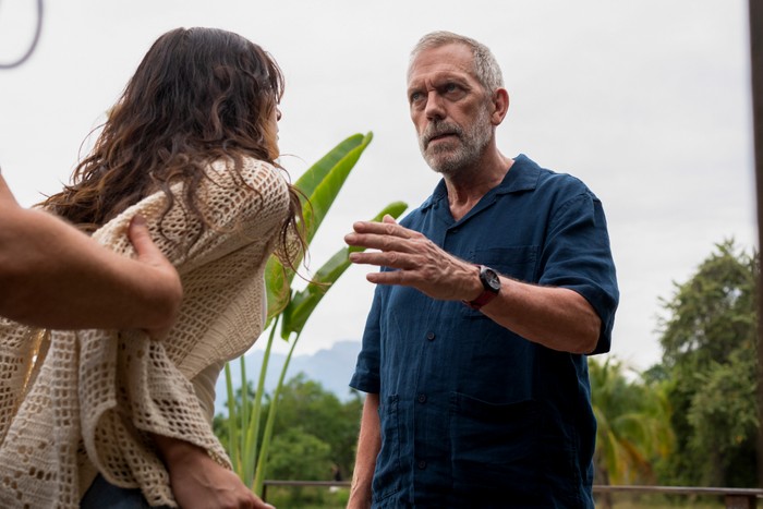 Camila Morrone and Hugh Laurie star in The Night Manager season 2; in this scene, Roxana is being restrained by someone out of frame, while Roper talks to her and gestures with his hand