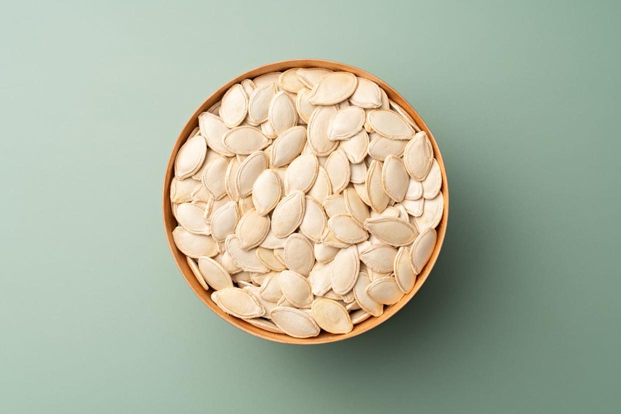 raw white pumpkin seeds in wooden bowl on green background