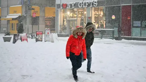 Getty Images Two people, dressed in thick coats, walk through the snow in New York City