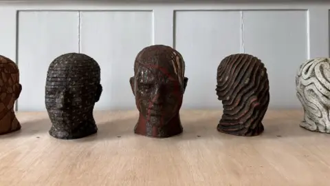 Joseph Hillier Sketches and maquettes of Joseph Hillier's head busts for the art train in Watlington. All five of them have different designs and are placed on a wooden table in a room.