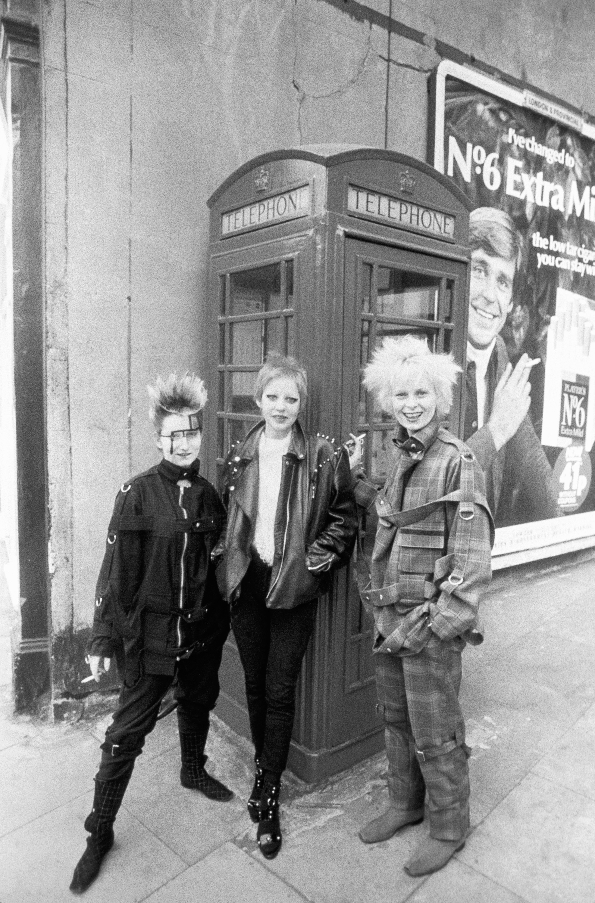 Black and white photo of Vivienne Westwood with spiky blonde hair with two people in punk outfits in front of a phone booth