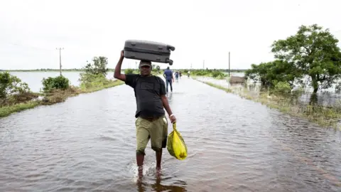 Reuters A man walks along a flooded road with a suitcase on his head