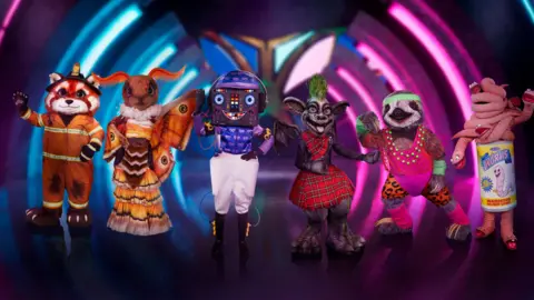 ITV Six masked characters on stage in the studio of the Masked Singer