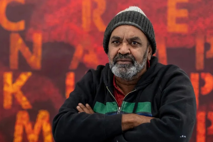 An Aboriginal man wearing a beanie with his arms crossed over his chest.