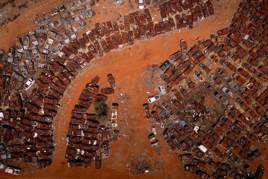 Piles of rusted cars on the ochre sand around it. Shot taken from above using a drone. 