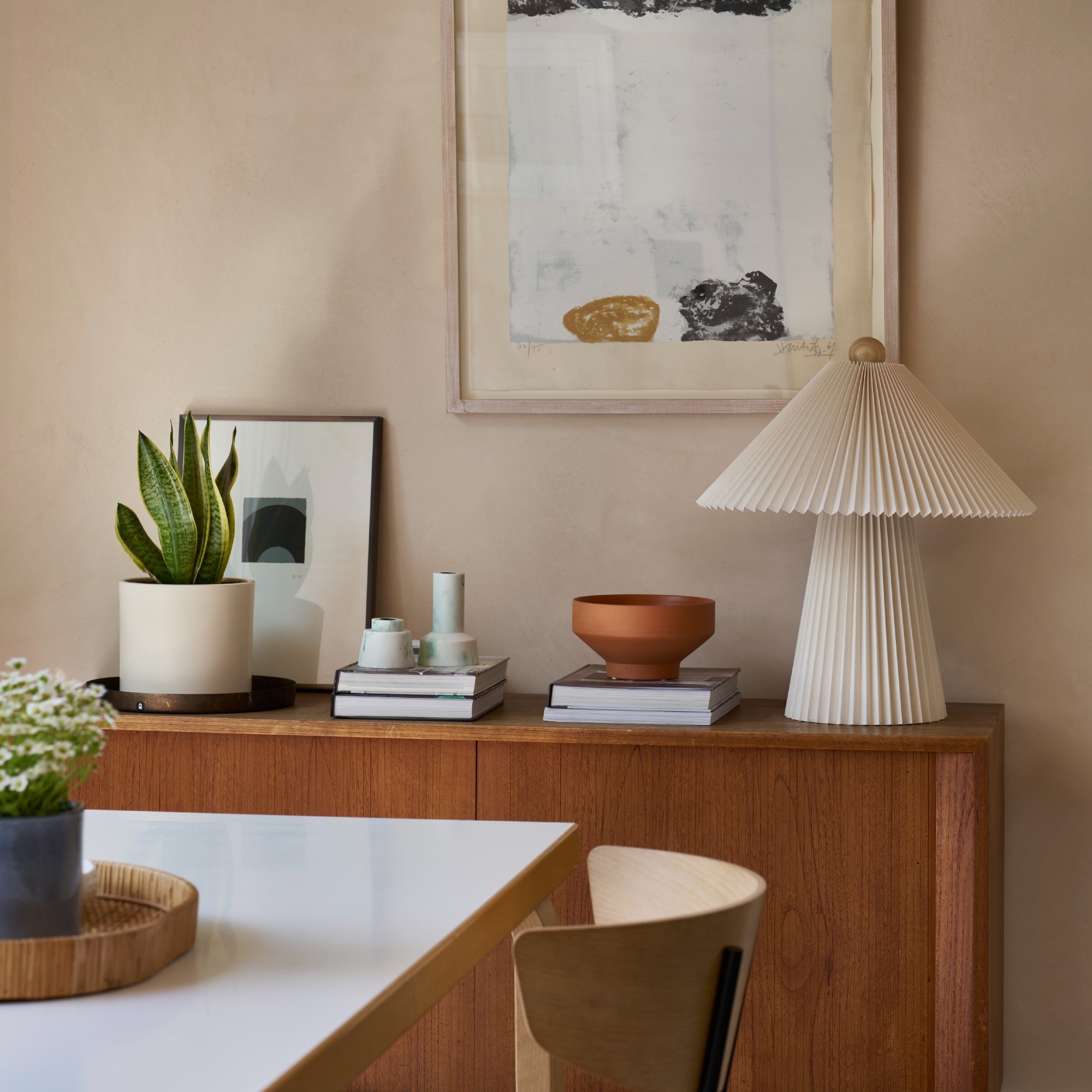 A wooden sideboard against a limewash wall with a pleated paper table lamp on top