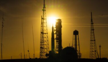 A silhouette of a rocket surrounded by scaffolding is seen in a dim yellow sunset