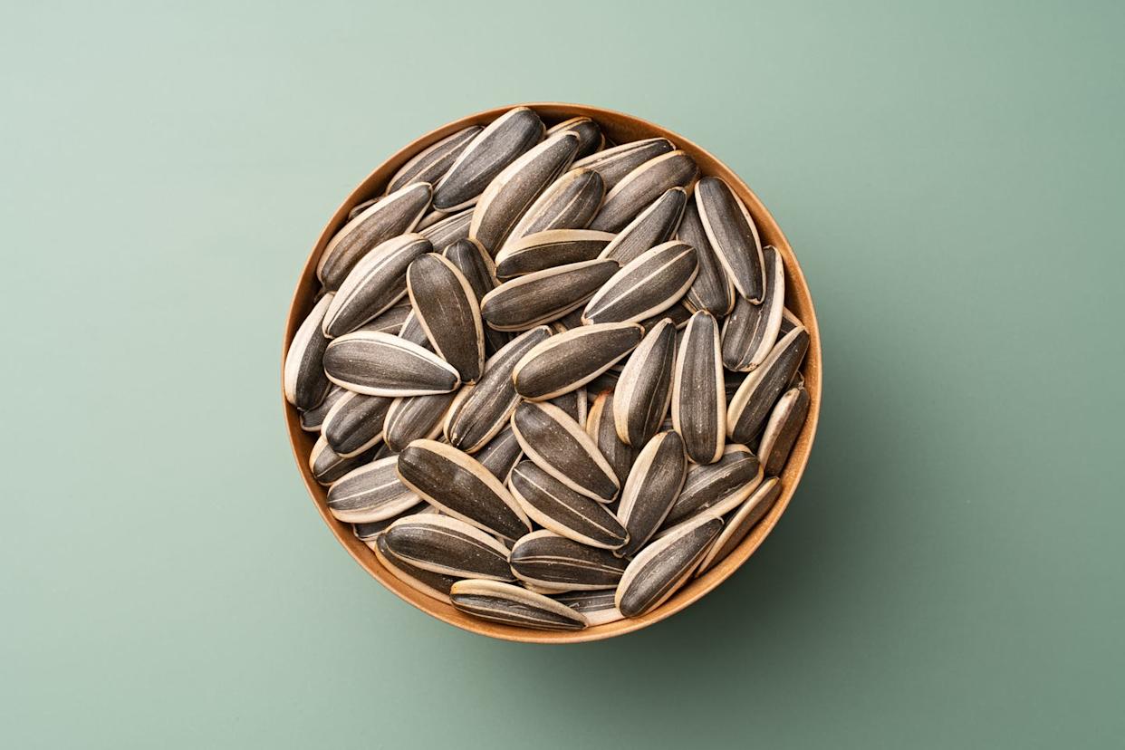 whole sunflower seeds in wooden bowl on green background