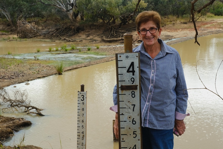 A woman stands next to a 4-metre flood marker beside a river.