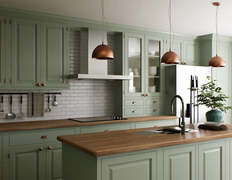 Modern kitchen with green cabinets, wooden countertops, copper pendant lights, and a central island. A potted plant sits on the island