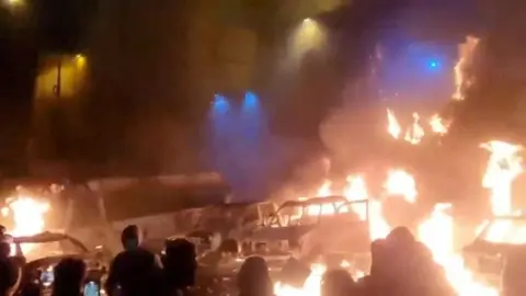 Reuters A screen grab of a video shows protesters standing near burning vehicles in the dark in Tehran, Iran.