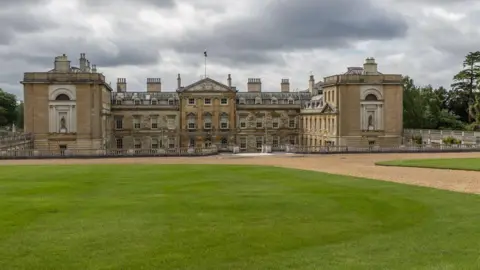 Christine Matthew/Geograph The picture shows Woburn Abbey, a large stately home, with a main section, two wings, and a grass area in front. There are a number of windows on the building, and a large roof area. 