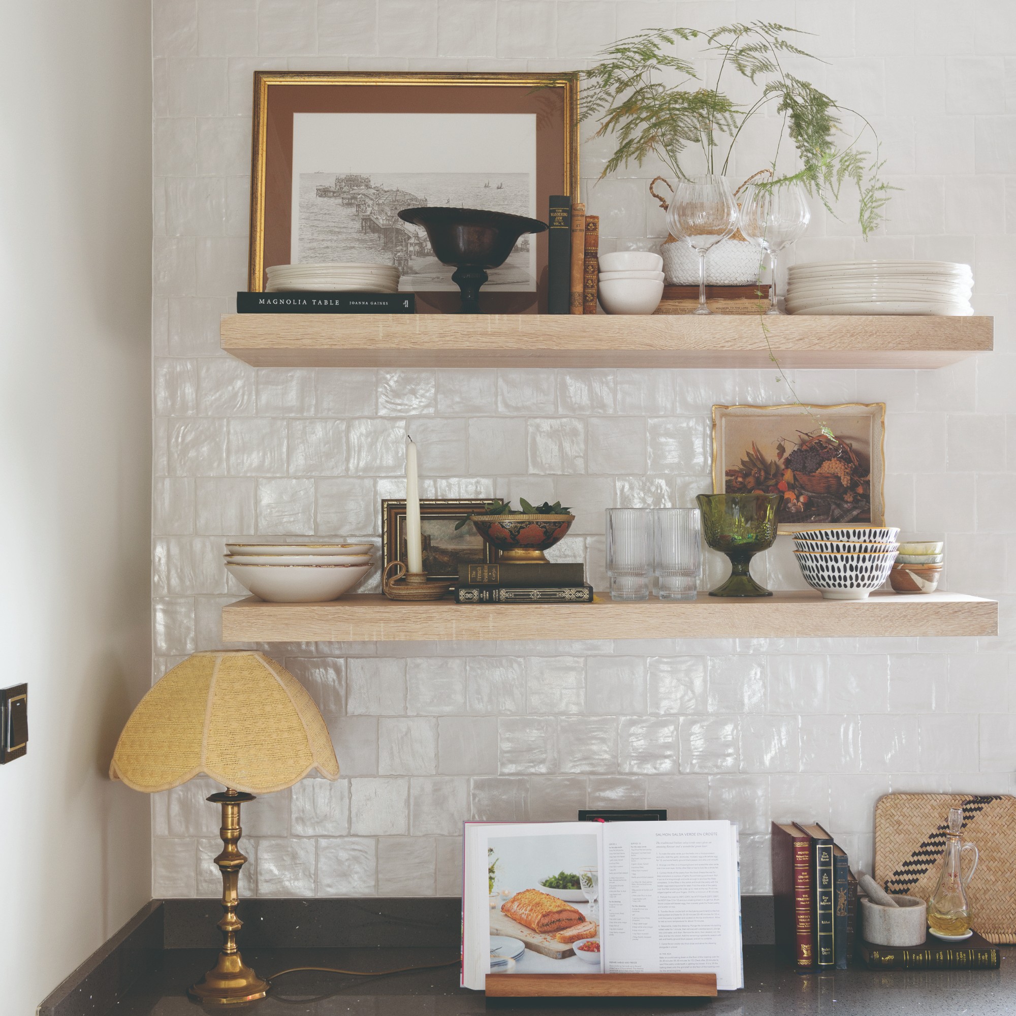 Kitchen shelves displaying tableware with vintage framed art and a fern houseplant